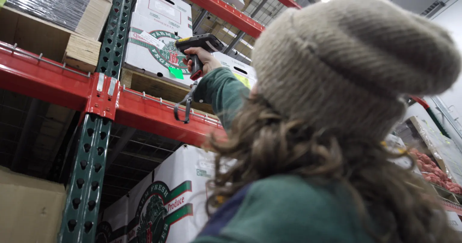 Worker scanning inventory in organic warehouse storage with shelving racks.