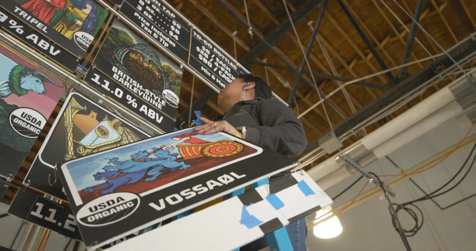 Worker hanging colorful USDA Organic beer signs in a production space