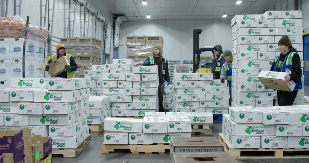 Warehouse crew in high-visibility vests handling cases of organic pears.